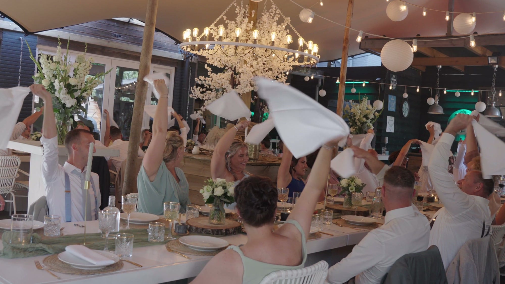 Gasten zwaaien met servetten tijdens het diner, uit de trouwfilm van Romy en Marijn