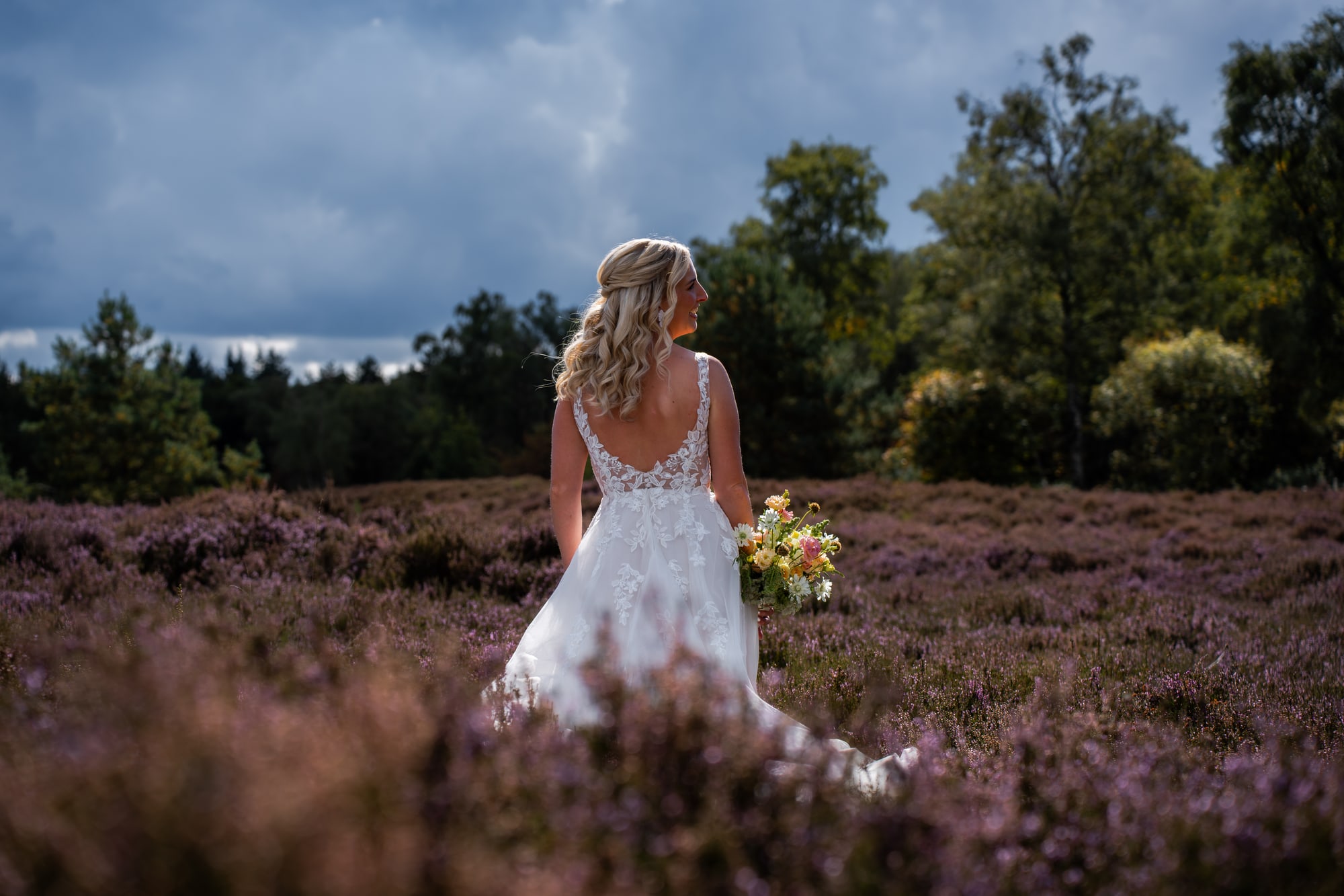 De bruid loopt over de bloeiende heide, het boeket in de hand